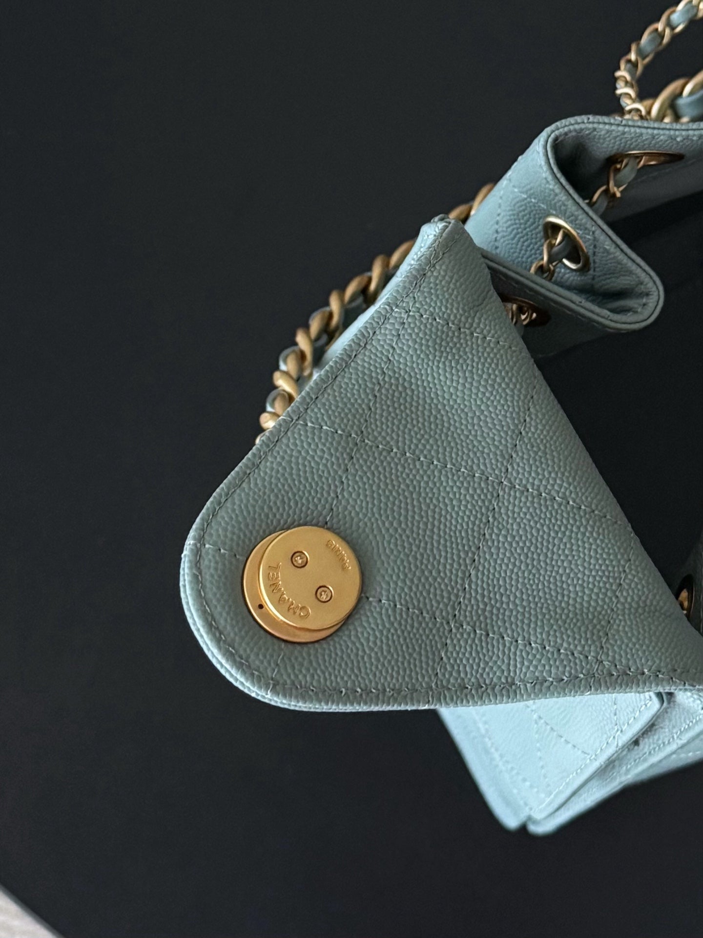 Chanel bag detail: light blue exterior with round gold snap and chain hardware