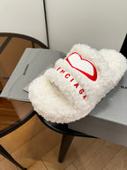 Sherpa slide sandals with red logo on white fuzzy strap, on gray dust bags
