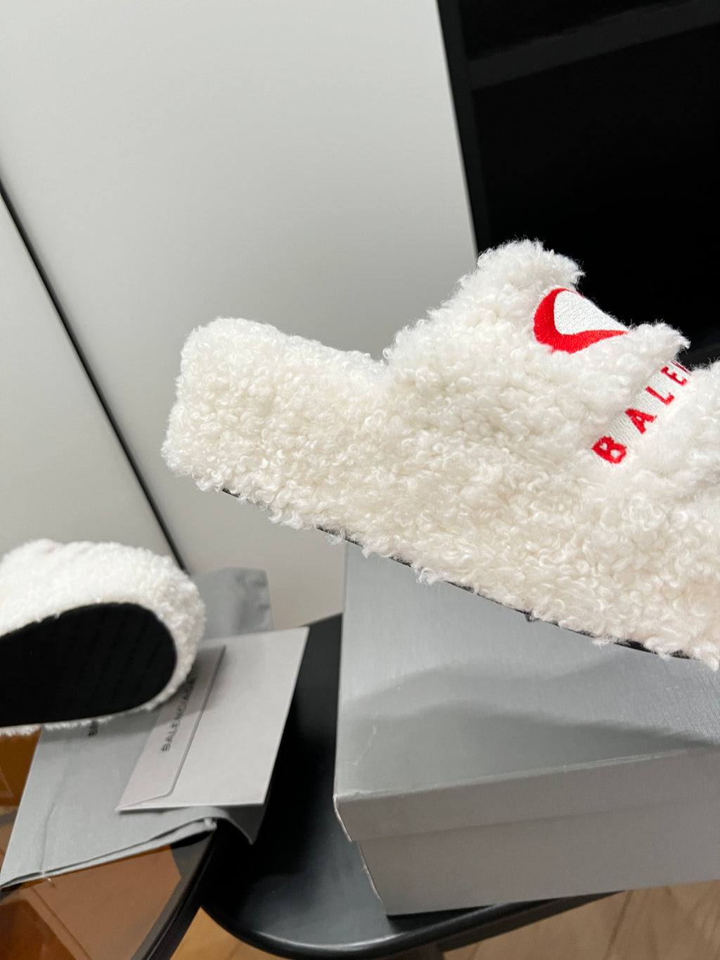 White sherpa slide sandal with red logo on fuzzy strap, side angle