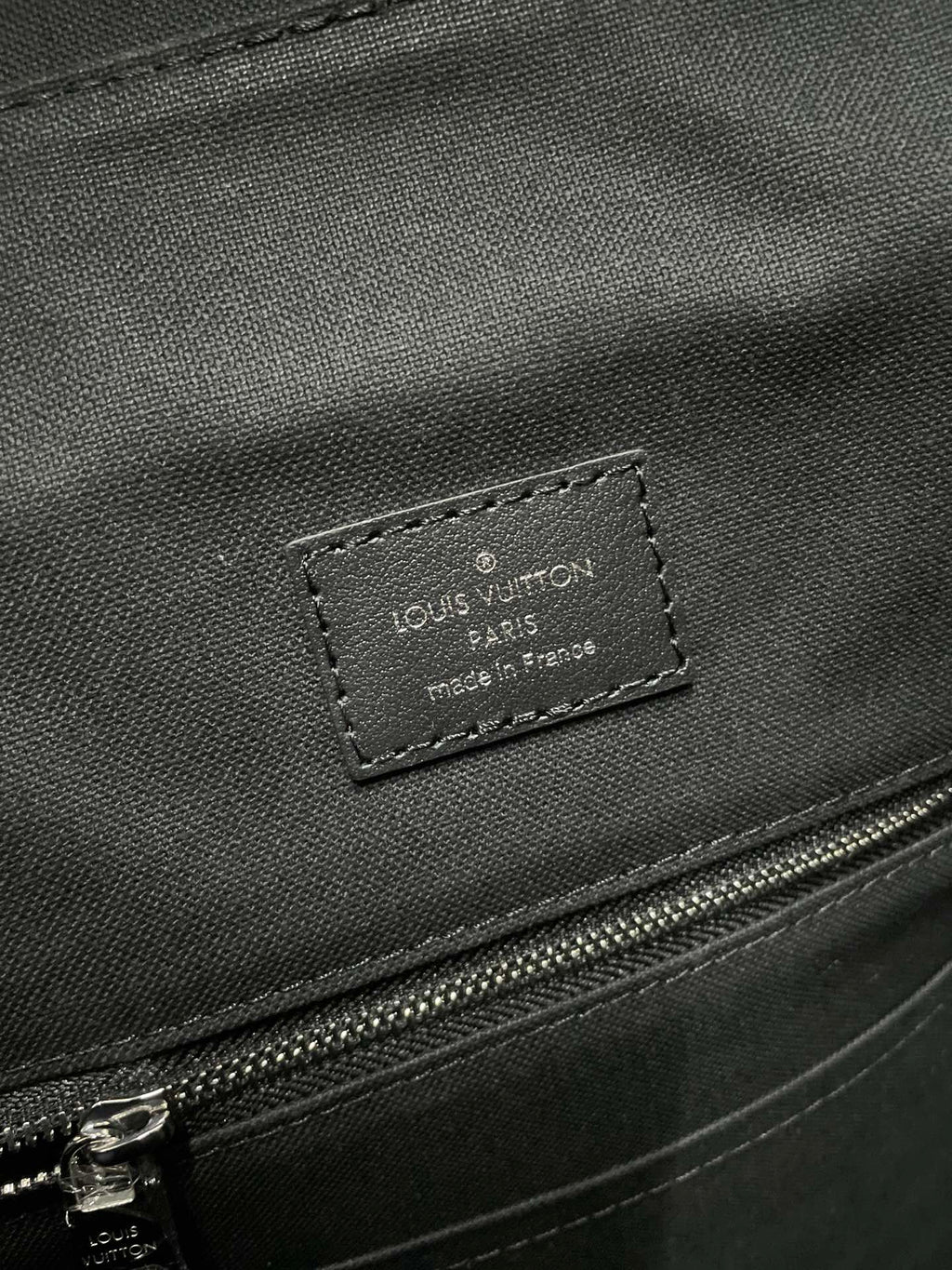 Louis Vuitton leather label on dark bag panel with stitched edge and zipper