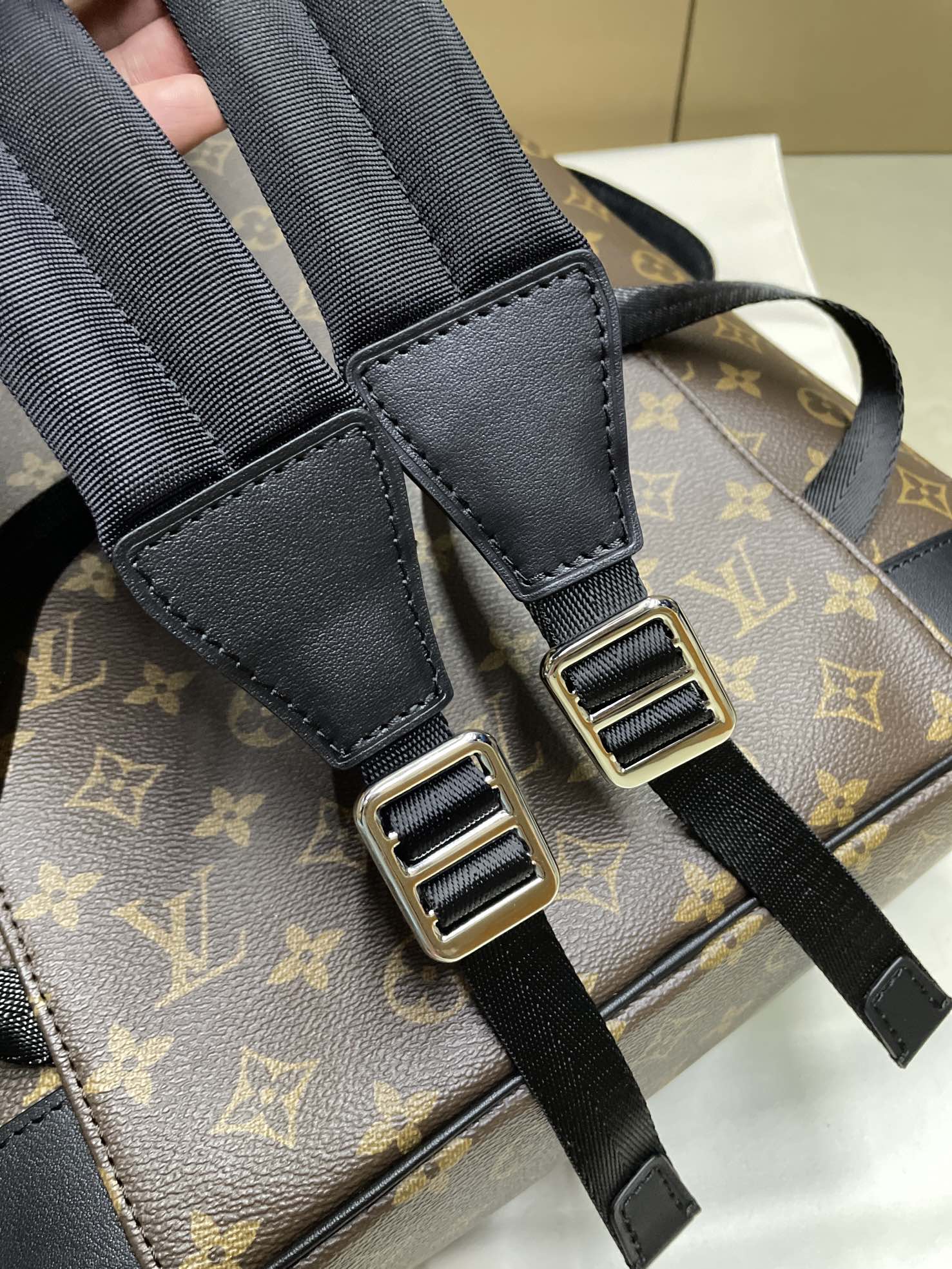 Adjustable black shoulder straps with metal buckles on Louis Vuitton monogram bag