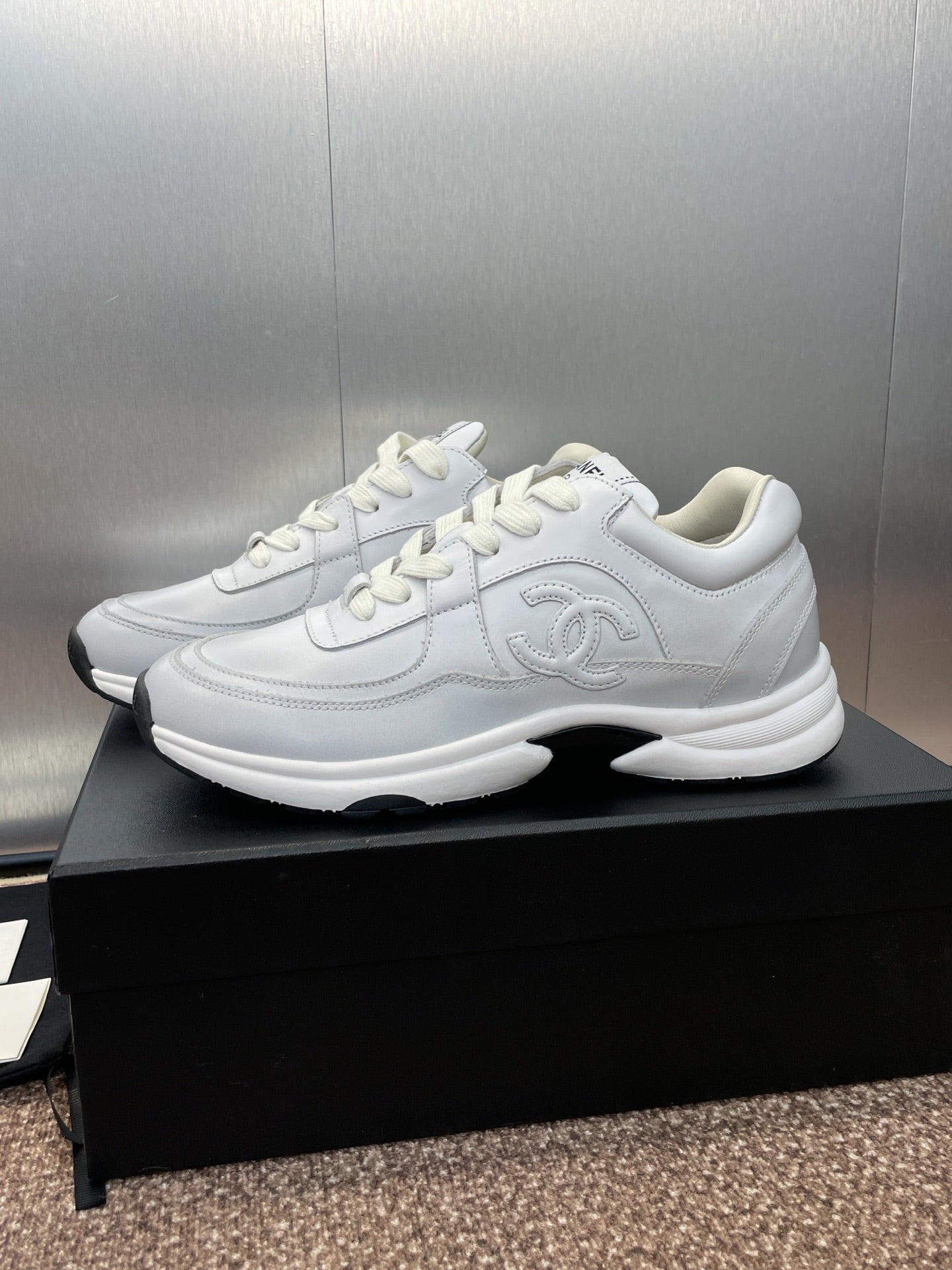 Chanel unisex white sneakers, angled top view on black box