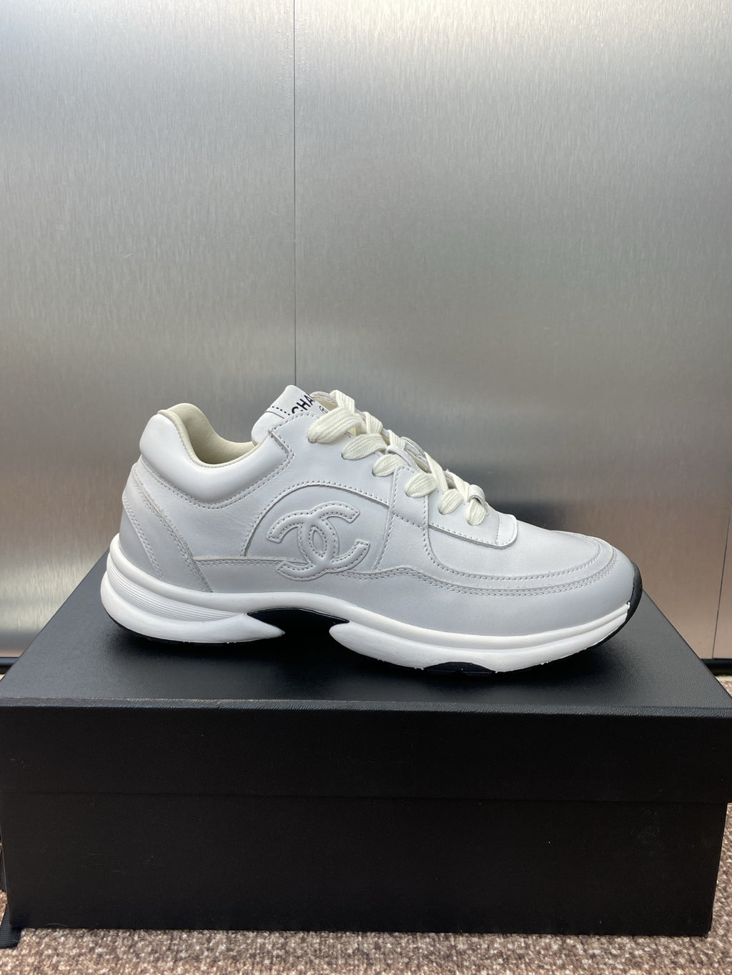 Chanel unisex white sneakers, side view on black box with logo detail