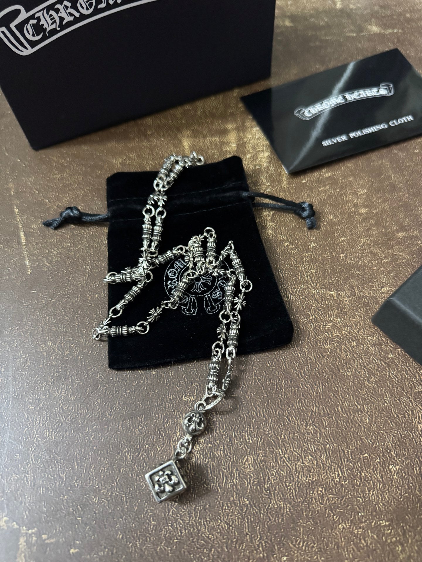 Silver-tone charm necklace with dangling square pendant over black drawstring pouch