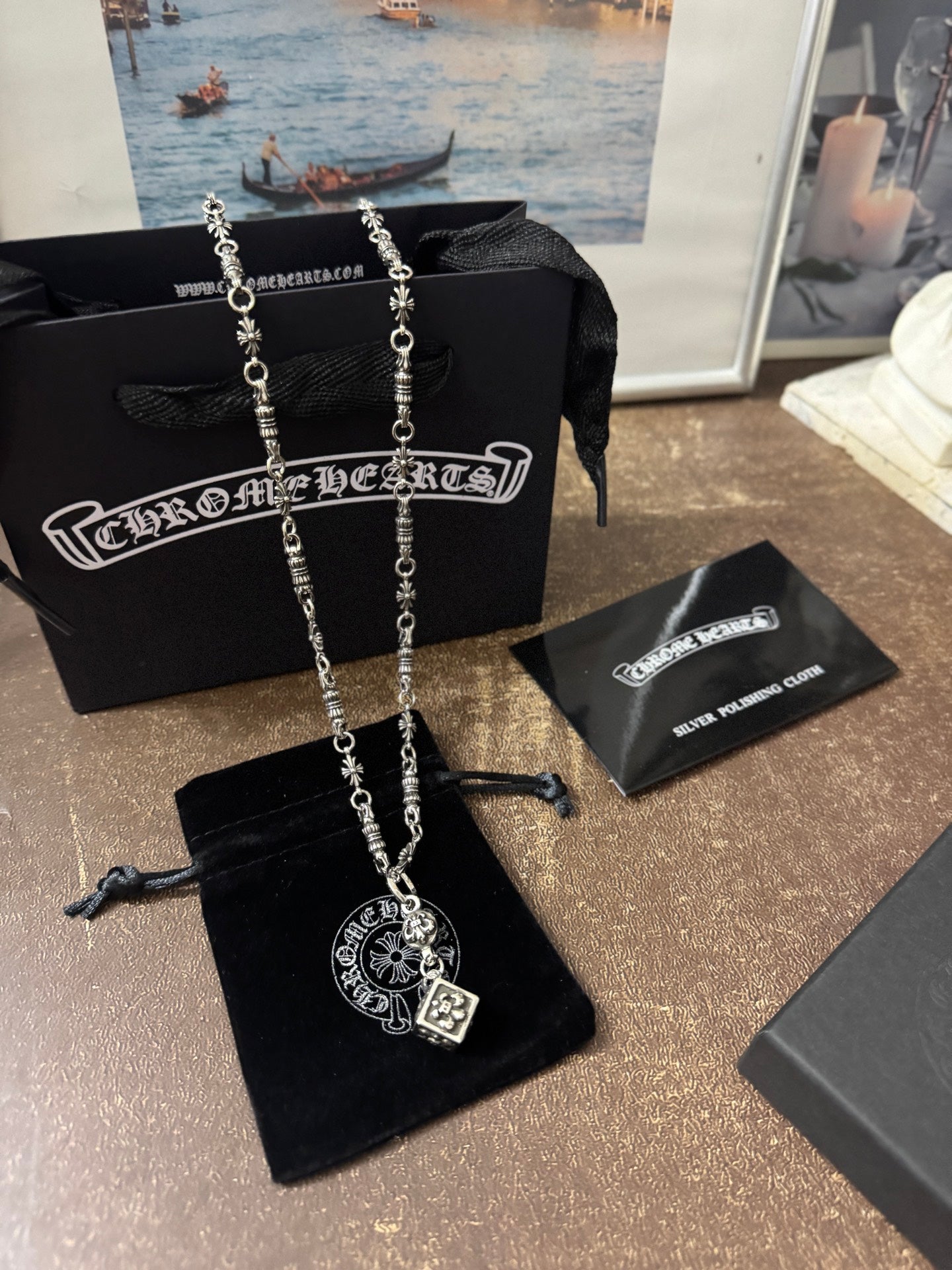 Silver-tone charm necklace with square pendant, packaged with black pouches and cards