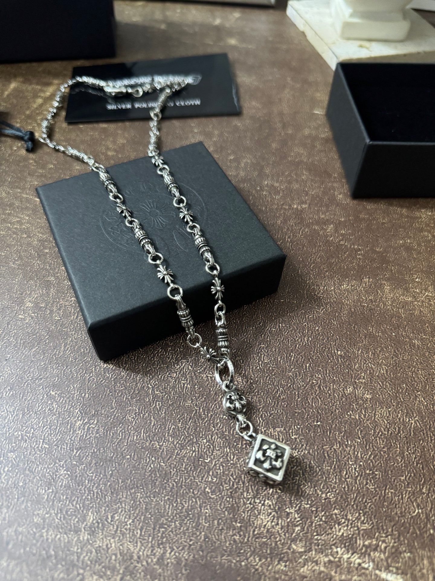 Silver-tone charm necklace with square pendant, shown on black jewelry box