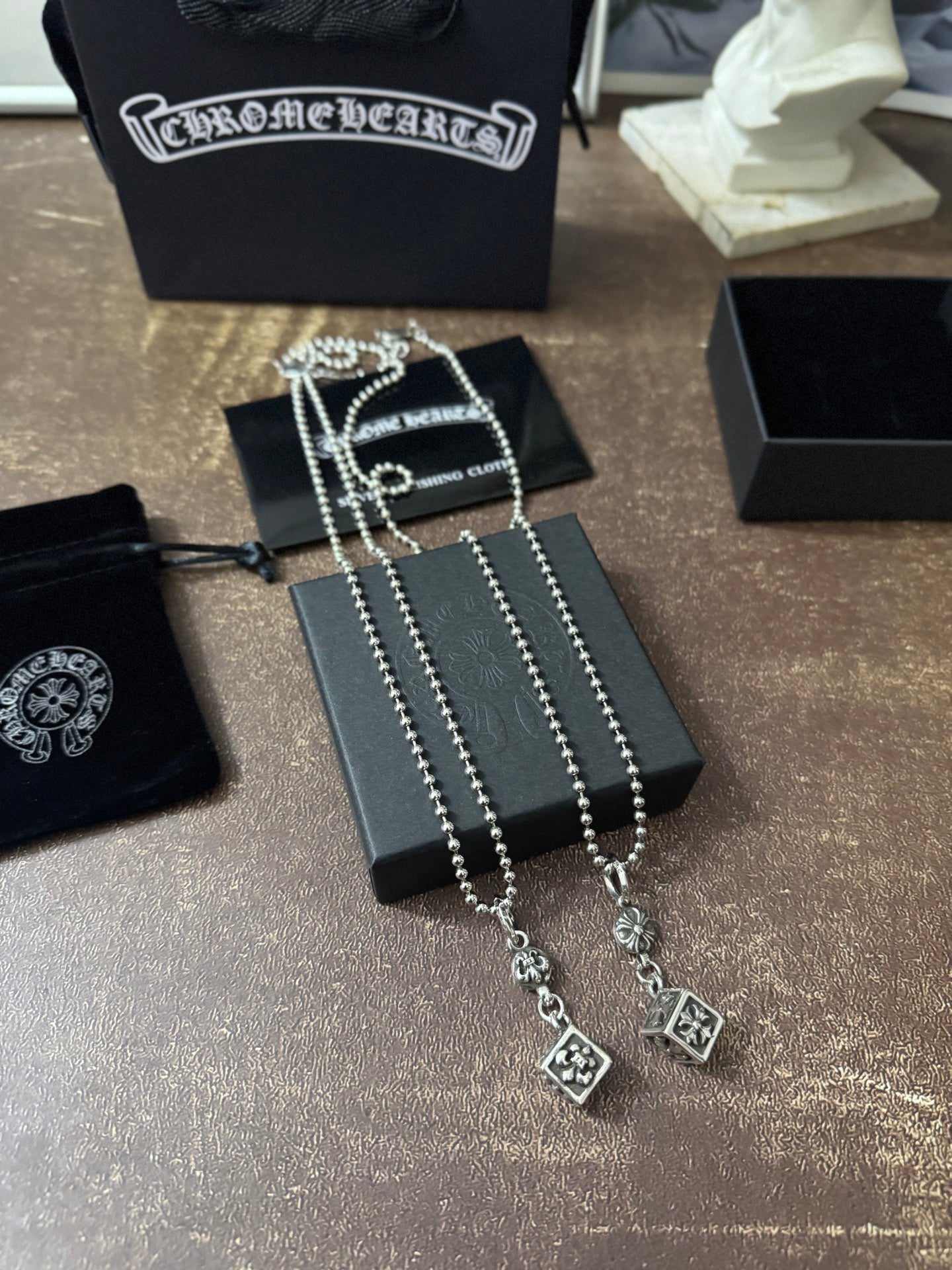 Silver-tone charm necklace set on display box with linked chains and square pendants.