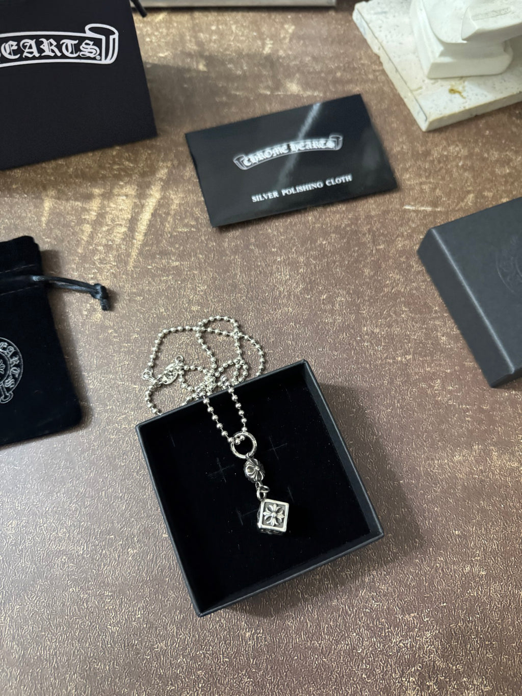 Silver-tone charm necklace with square pendant in black jewelry box, chain looped.