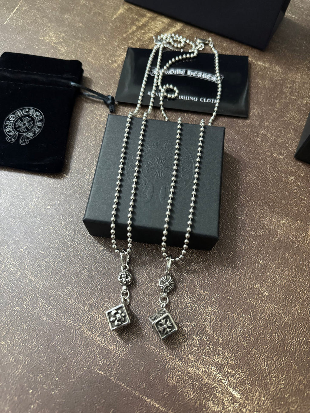 Silver-tone charm necklace with long chain strands and square pendant charms in box.