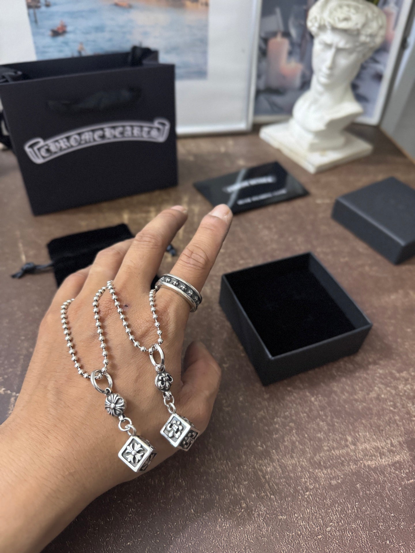 Silver-tone chain charm jewelry held in hand with square and round pendant charms.