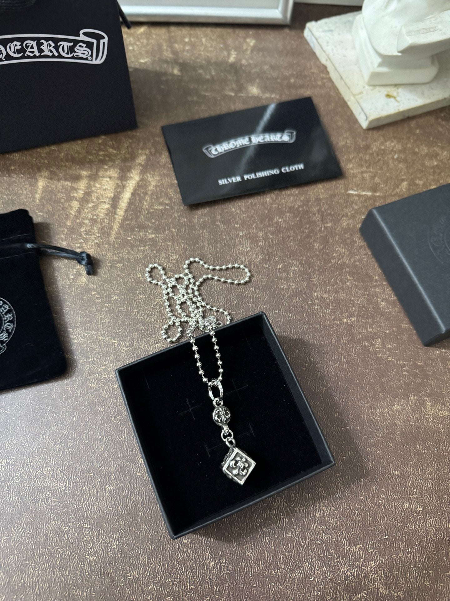 Silver-tone charm necklace with square pendant on black jewelry box with chain draped.