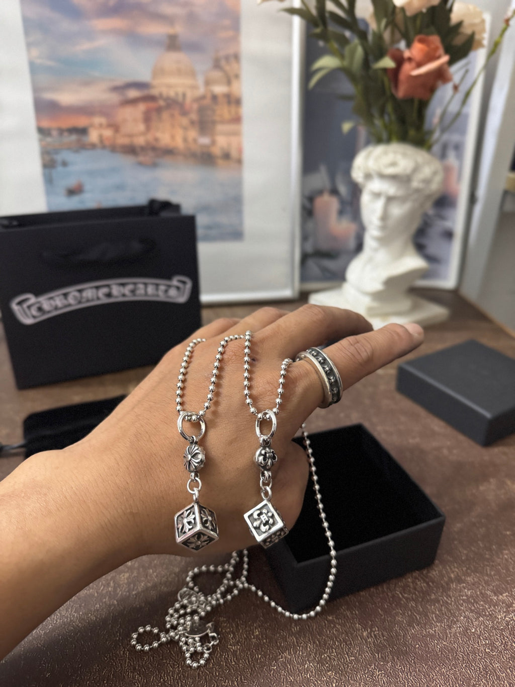 Silver-tone chain charm necklaces in hand with square and round pendants and long chain.