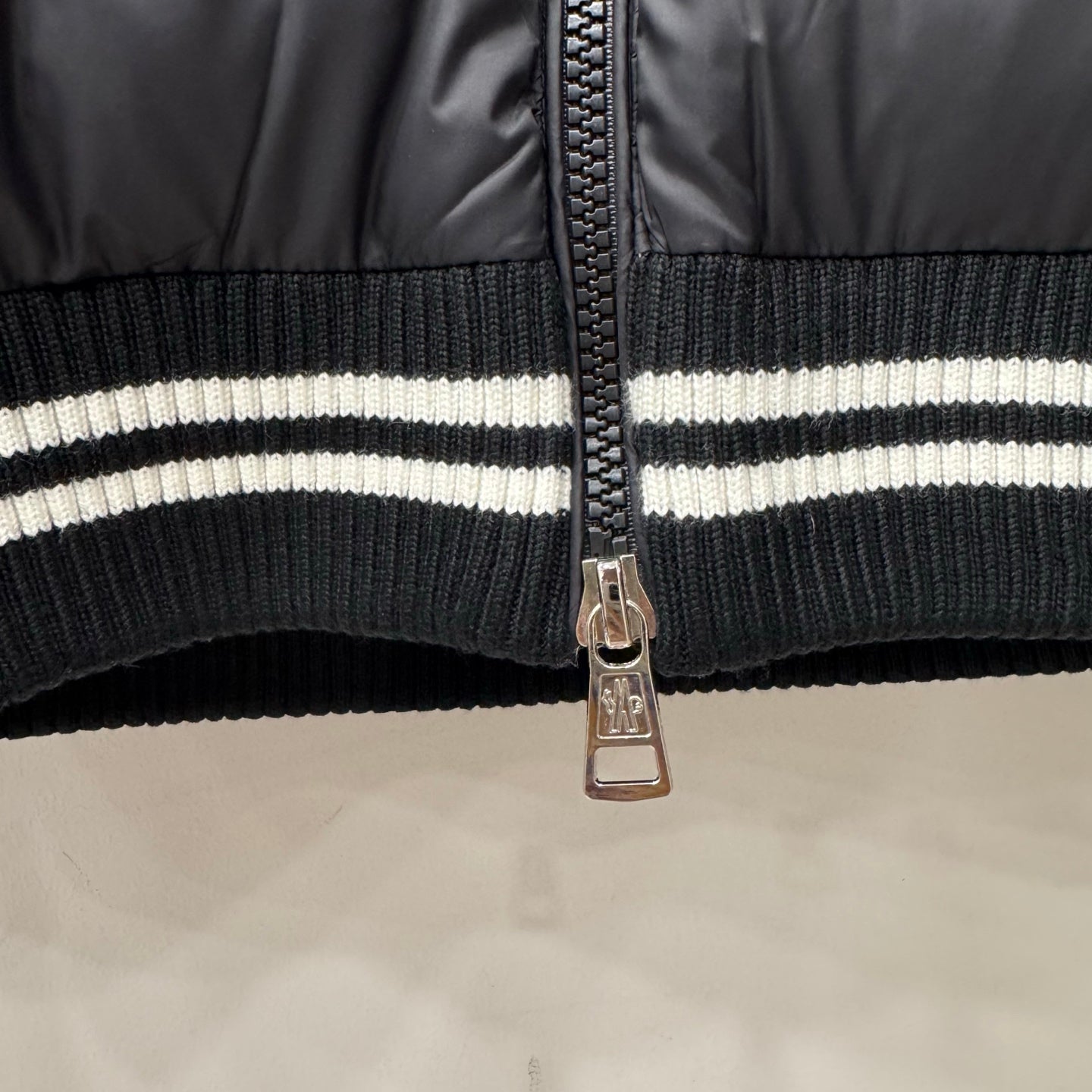 Metal front zipper on ribbed striped waistband of dark puffer jacket