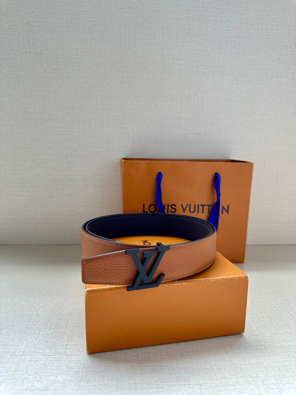 Louis Vuitton leather belt with LV buckle, tan strap on top of orange box