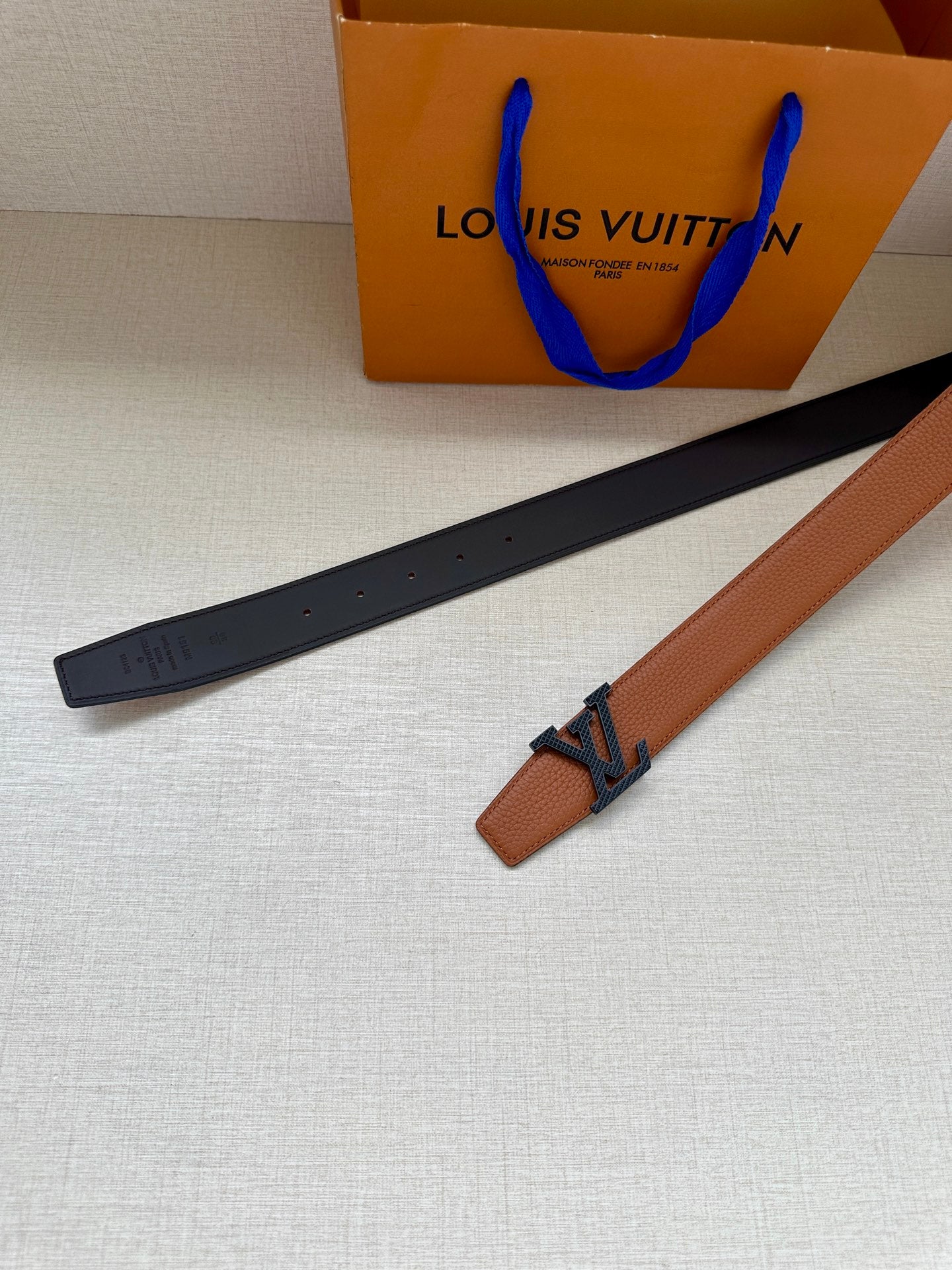 Louis Vuitton belt laid flat, tan strap with LV buckle and dark backing