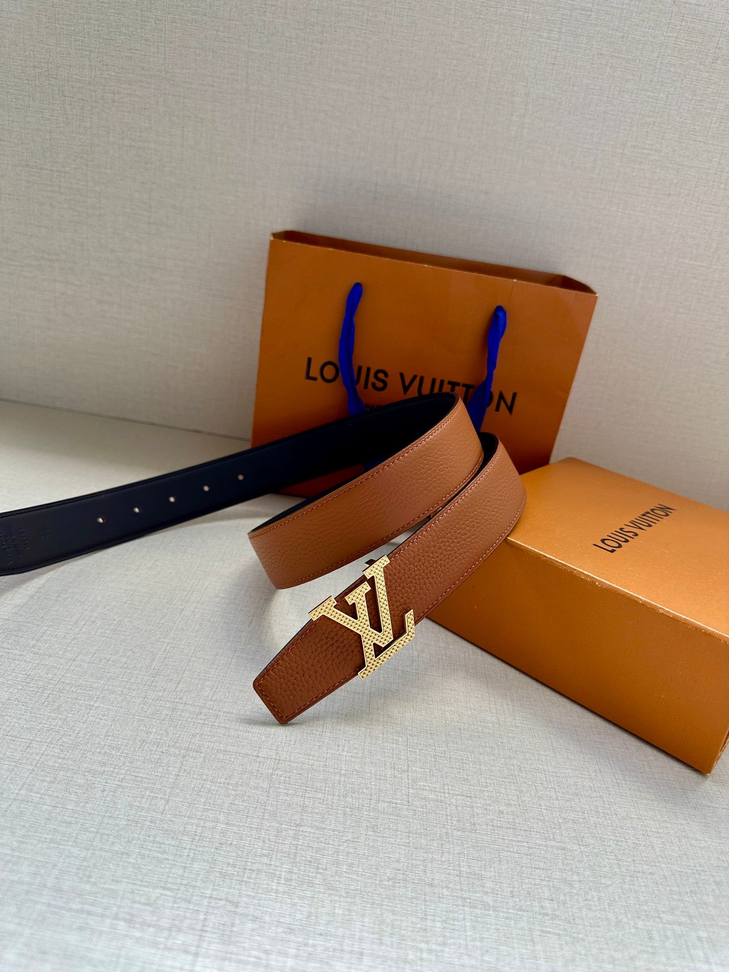 Louis Vuitton leather belt with LV silver buckle and tan strap, beside boxes