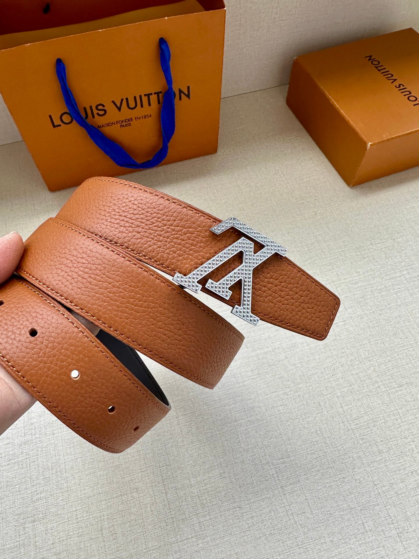 Louis Vuitton tan leather belt with LV silver buckle held in hand