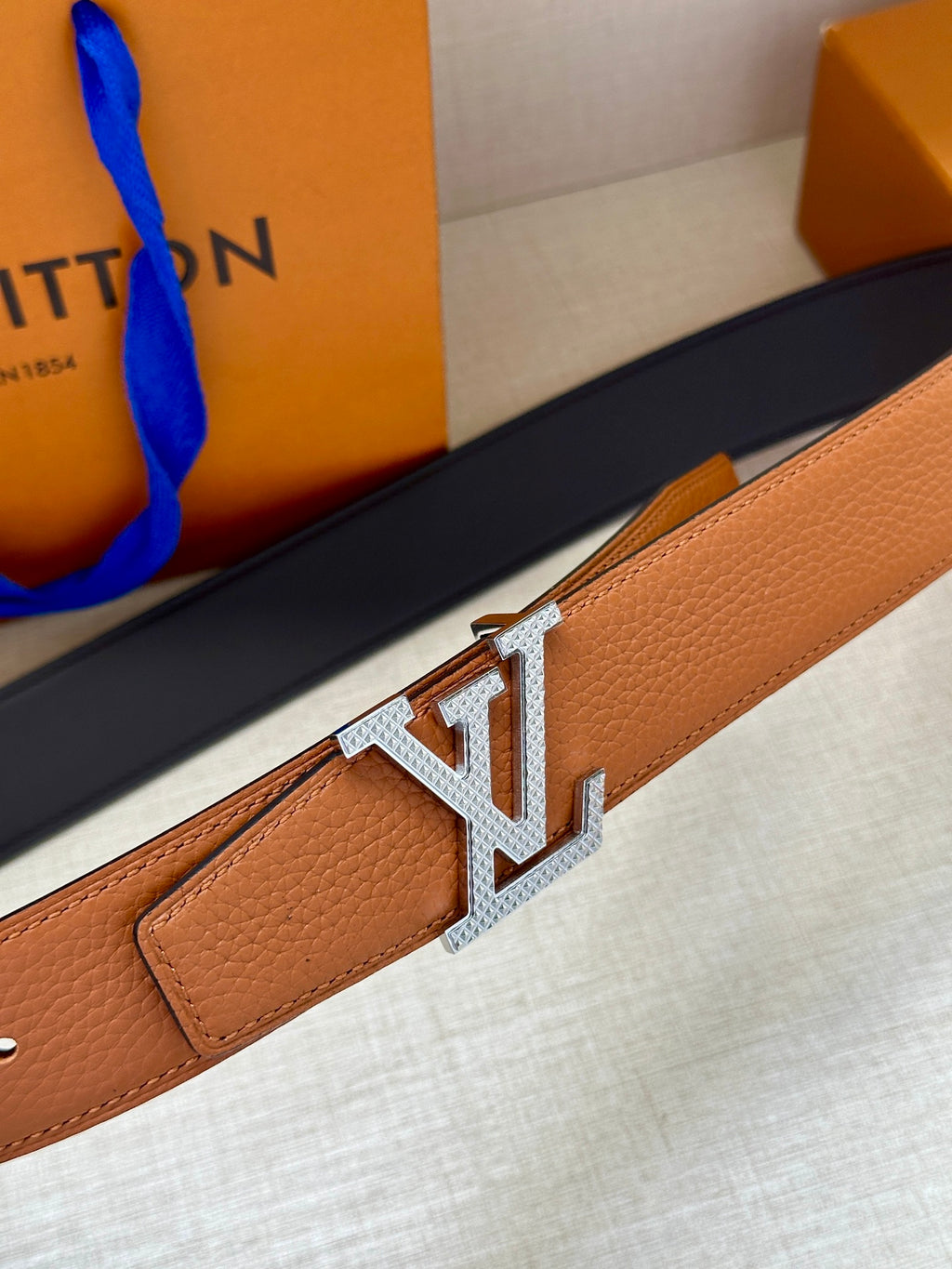 Louis Vuitton belt close-up with LV silver buckle on tan leather strap