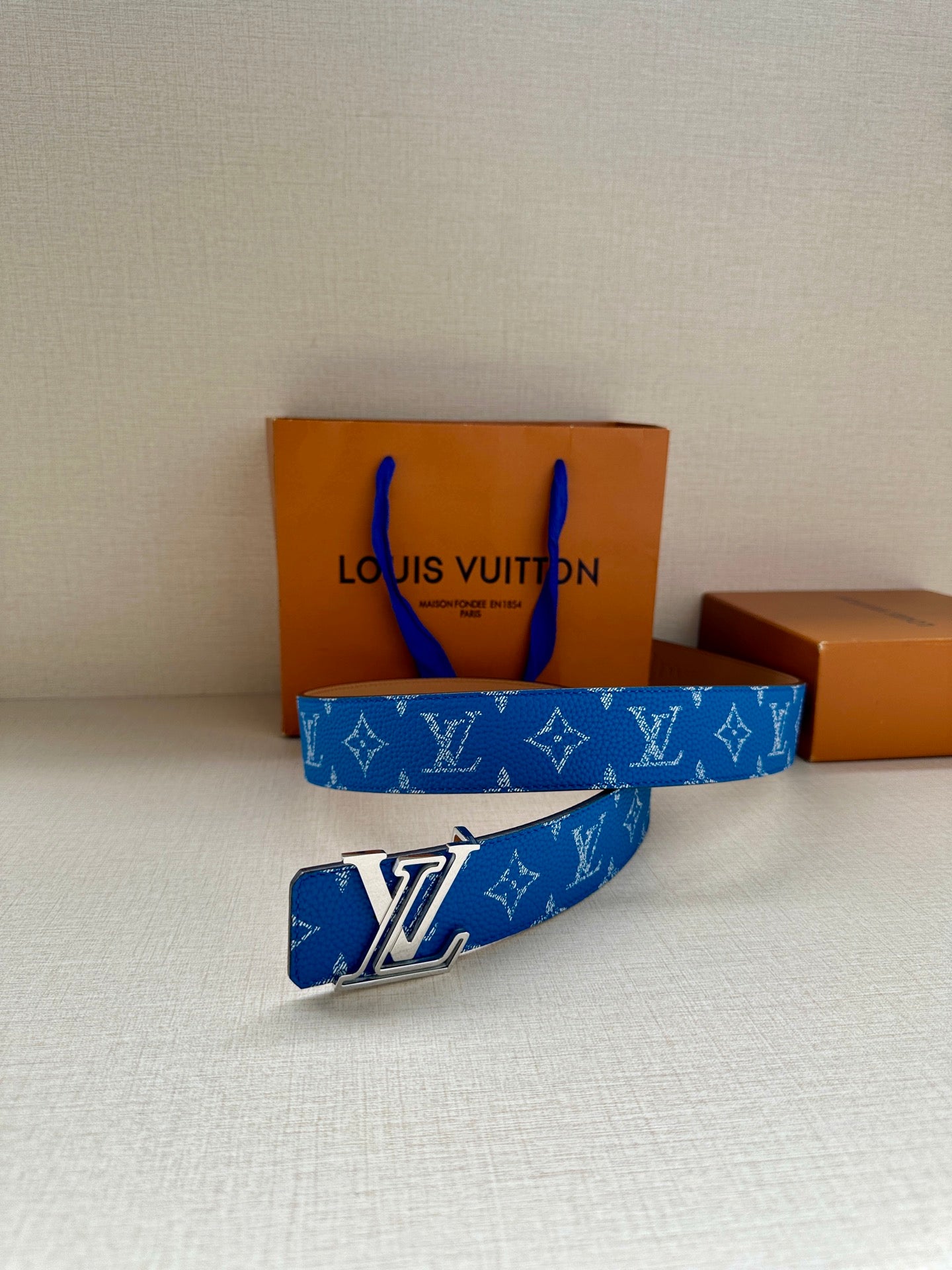 Blue Louis Vuitton belt with monogram pattern and silver LV buckle on display