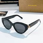 Bvlgari cat-eye sunglasses, dark frames, gray-tinted lenses, gold emblem bridge