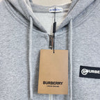 Gray zip hoodie close-up of chest and zipper with Burberry tag on hanger.
