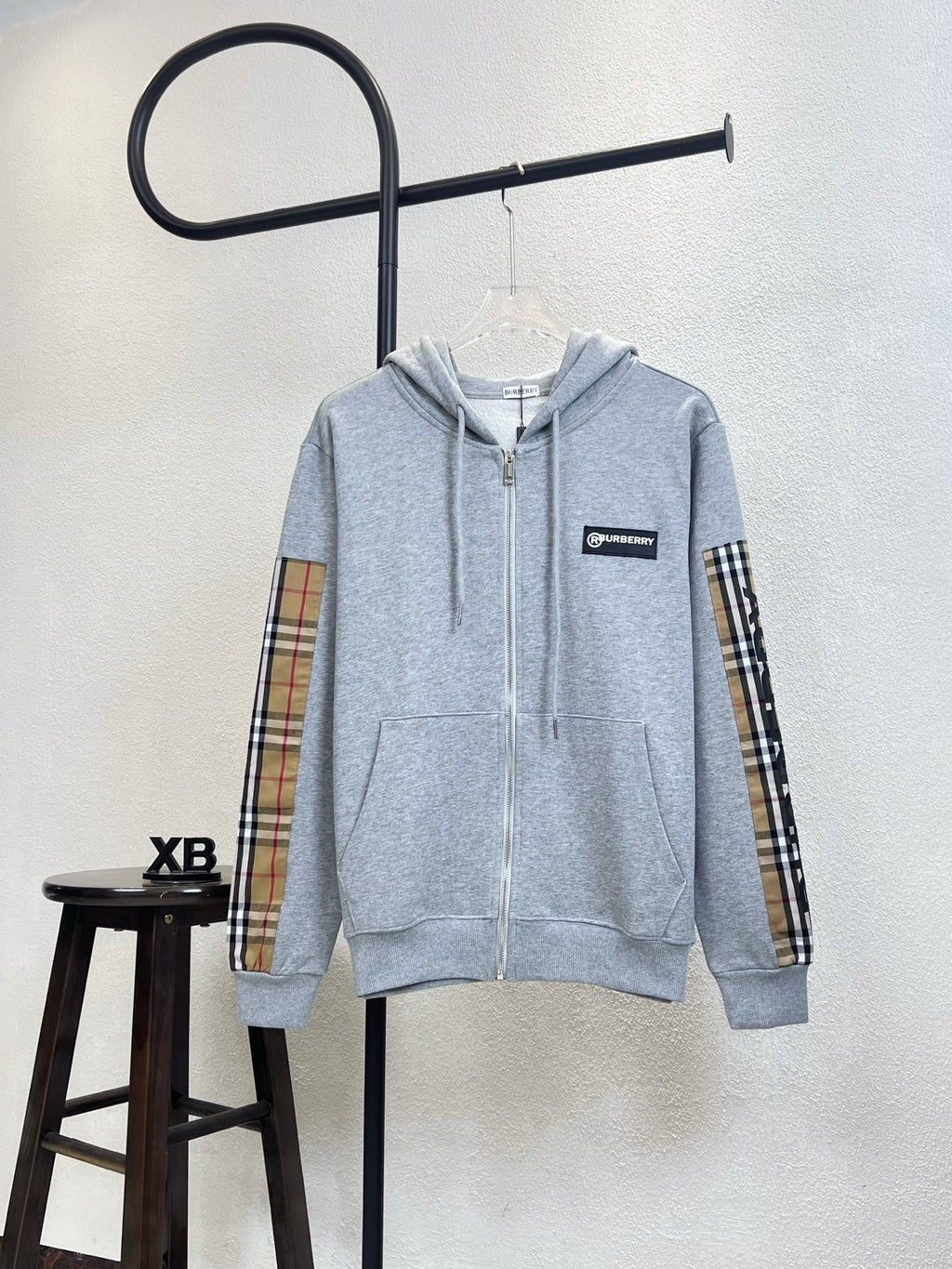 Light gray zip-up hoodie with hood, front zipper and plaid sleeve accents.