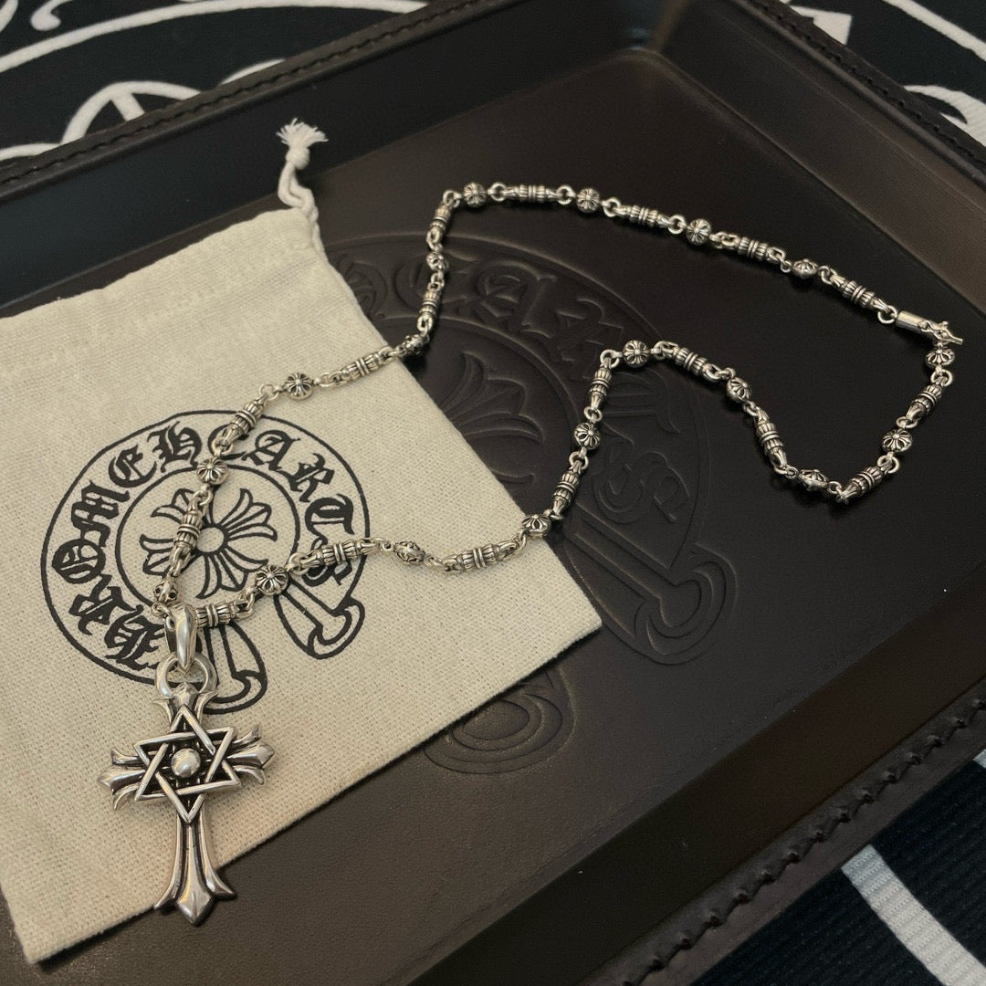 Silver-tone chain necklace with cross star pendant hanging beside a circular charm