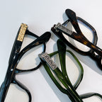 Assorted eyeglasses with dark, tortoise, and green frames and ornate hinge bars