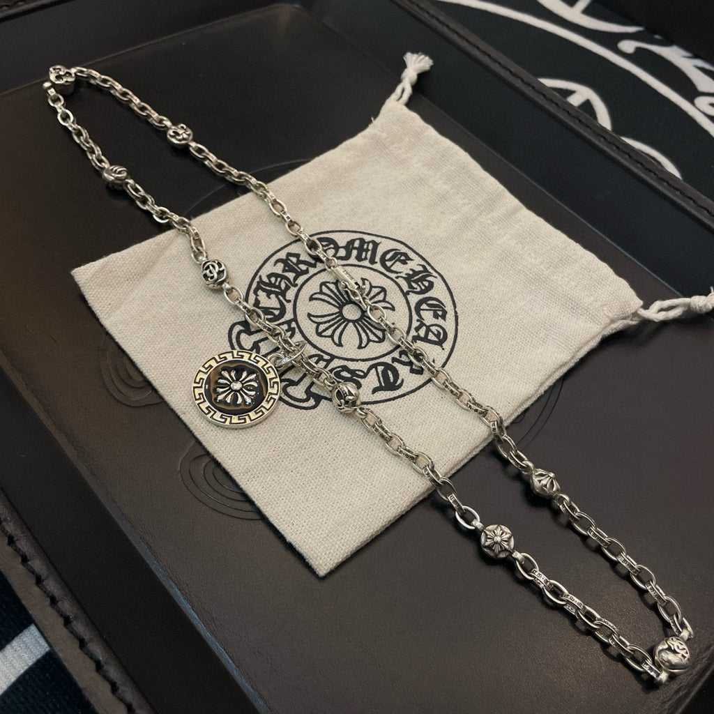 Silver-tone pendant necklace laid on a pouch with round sun medallion charm