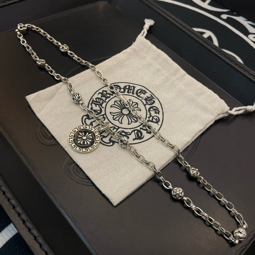 Silver-tone pendant necklace laid on a pouch with round sun medallion charm
