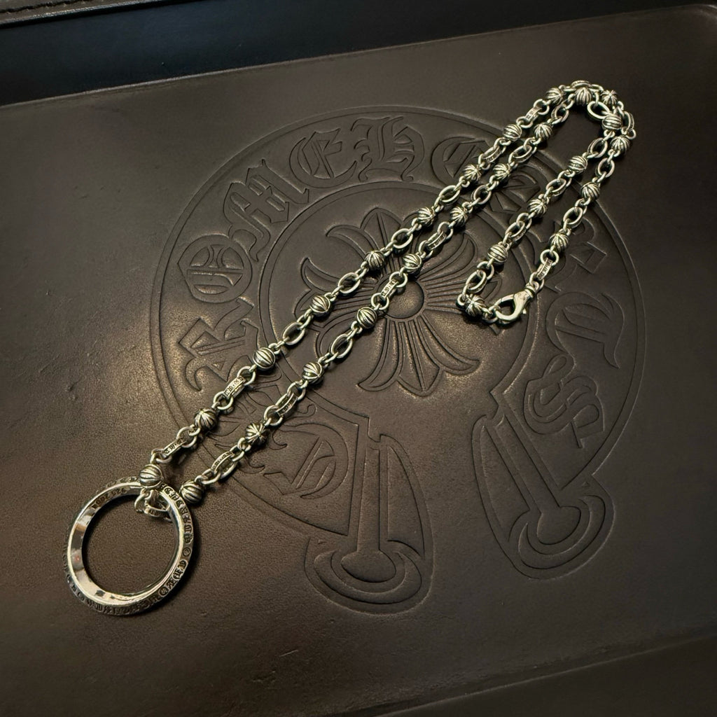 Silver necklace chain with large round ring pendant on dark leather-like board.