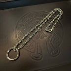 Silver necklace chain with large round ring pendant on dark leather-like board.
