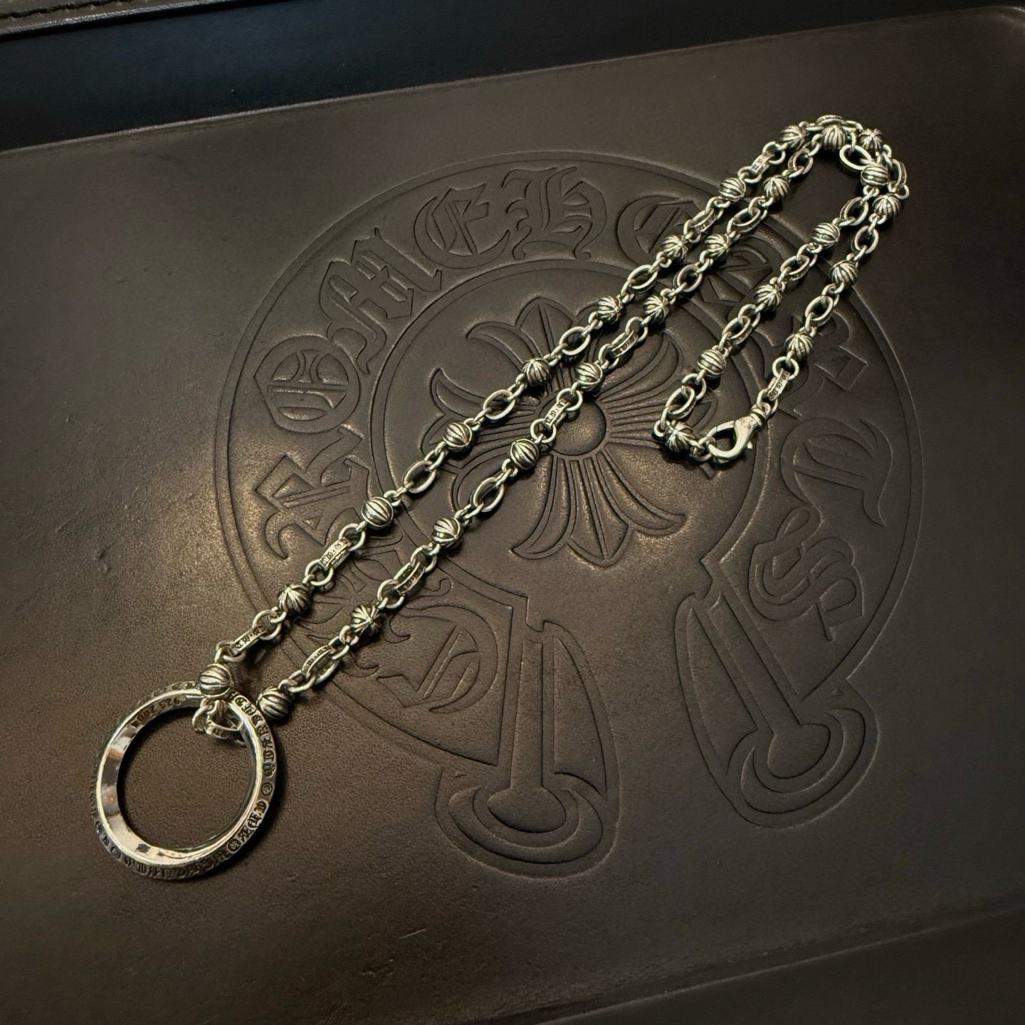 Silver necklace chain with large round ring pendant on dark leather-like board.