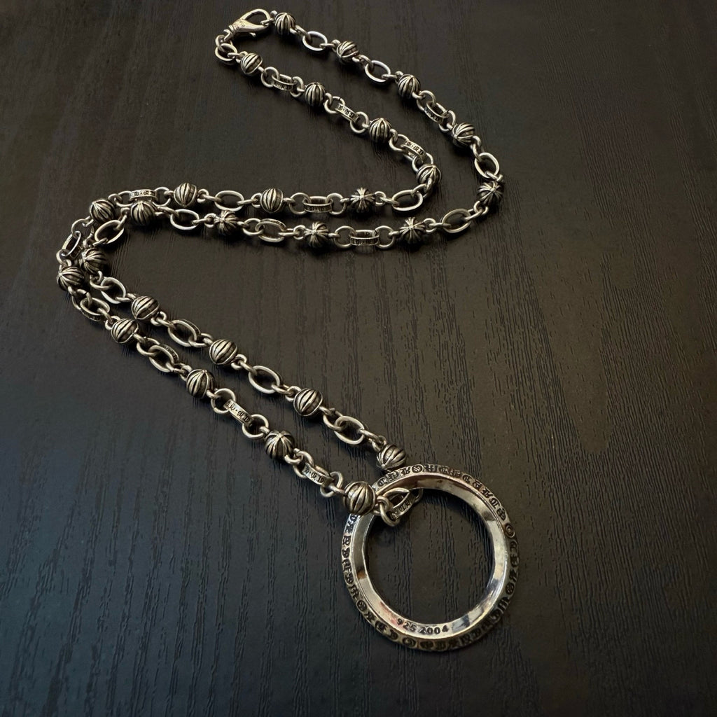 Silver chain necklace with large oval ring pendant on dark surface.