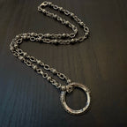 Silver chain necklace with large oval ring pendant on dark surface.