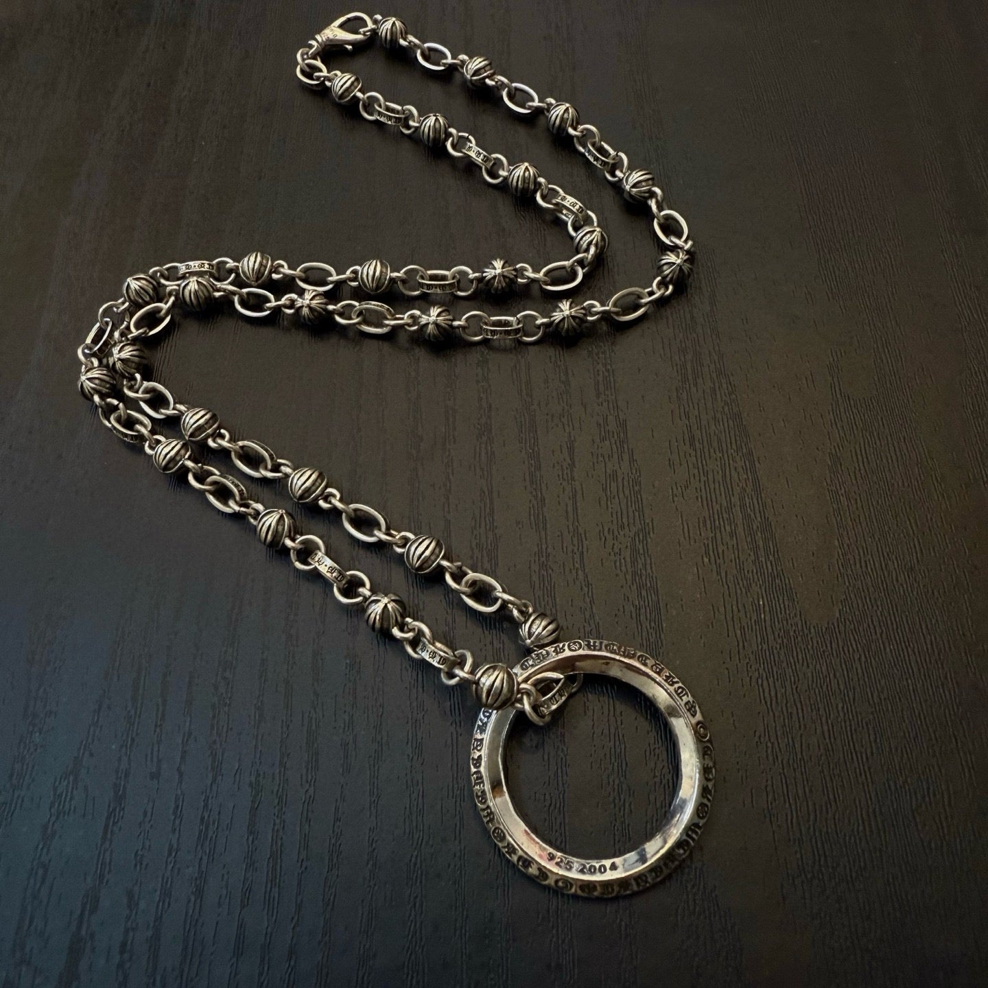 Silver chain necklace with large oval ring pendant on dark surface.