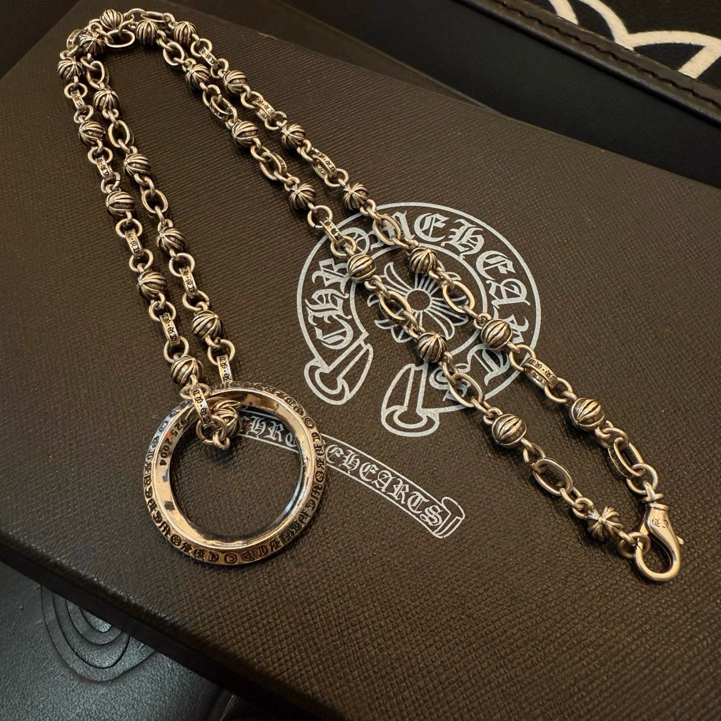 Silver charm necklace with circular ring pendant and long chain strand on box.