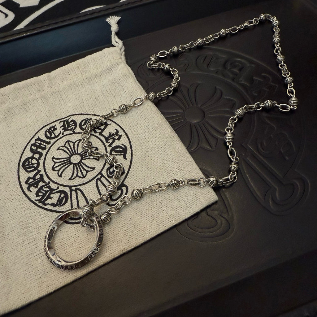 Silver chain necklace with round ring pendant and clasp on fabric pouch and box.