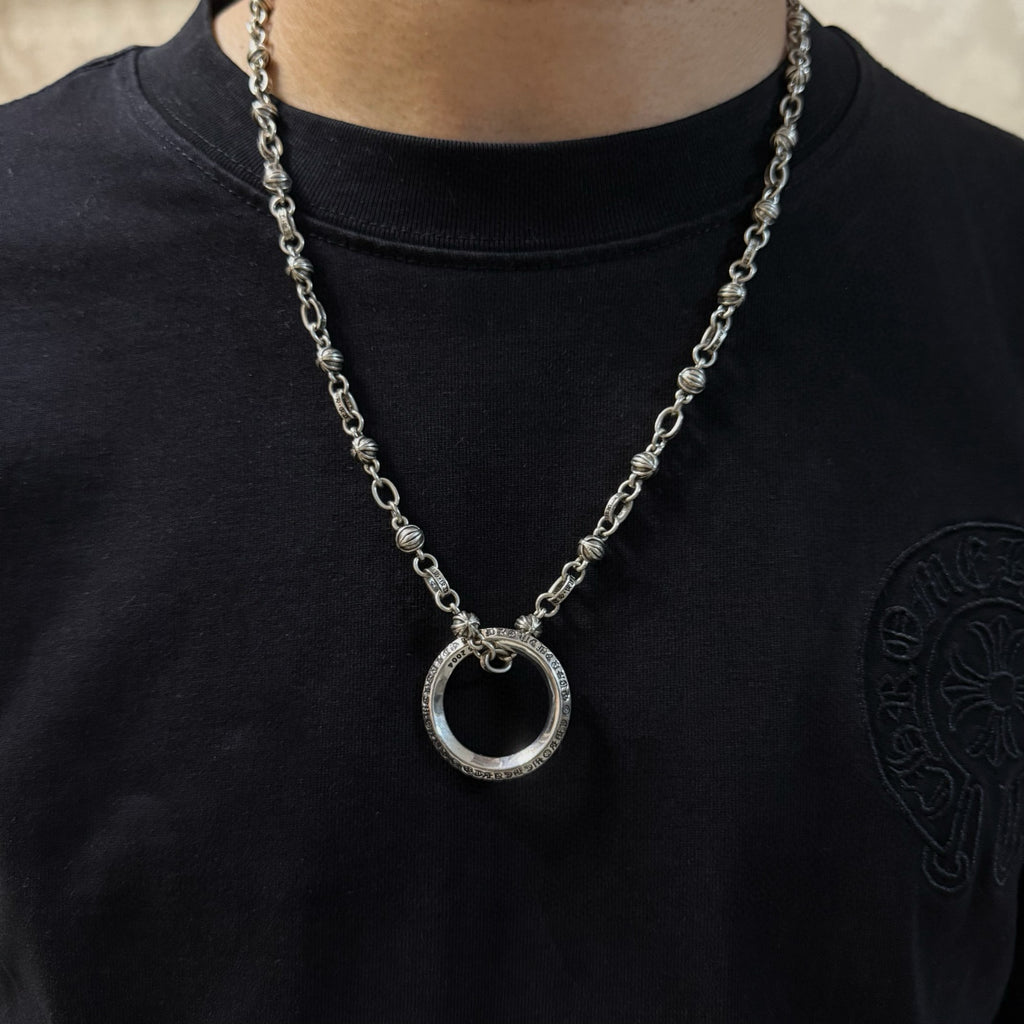 Silver ring pendant necklace worn with black crew-neck shirt.