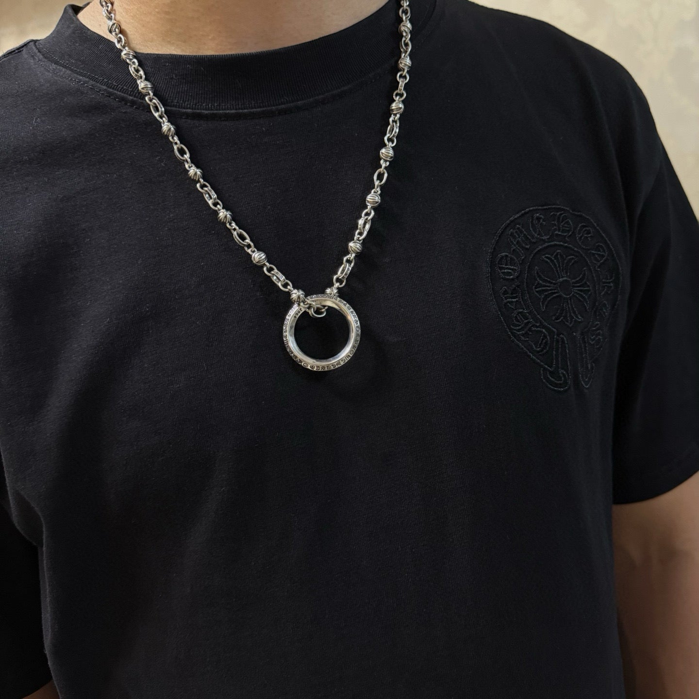 Silver ring pendant necklace worn on black T-shirt with small chest emblem.