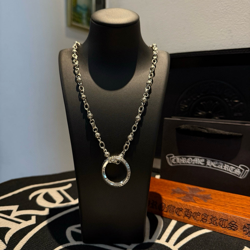 Silver chain necklace with round ring pendant, layered links on black display bust.