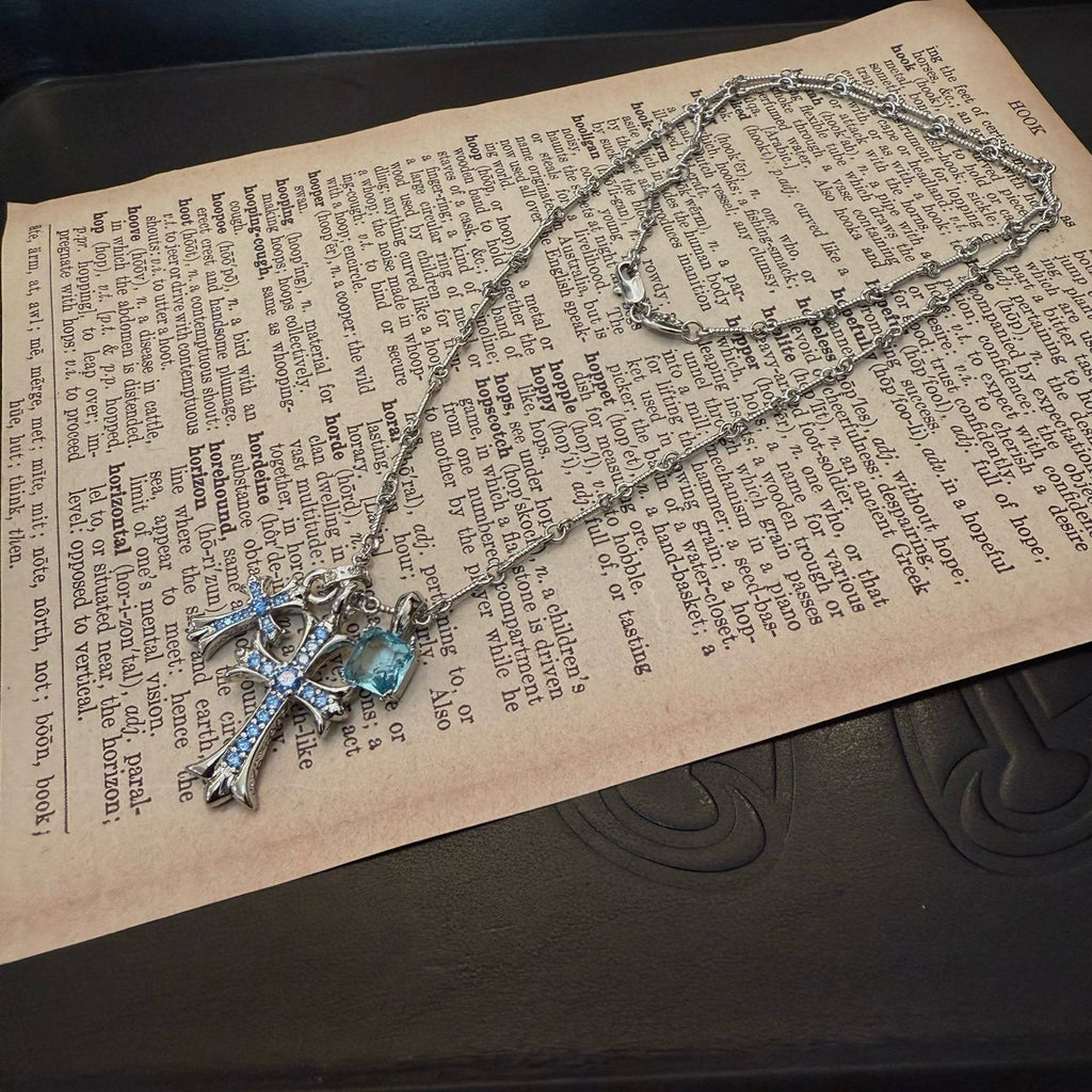 Silver cross pendant necklace with blue gemstone details laid on text pages