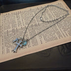Silver cross pendant necklace with blue gemstone details laid on text pages