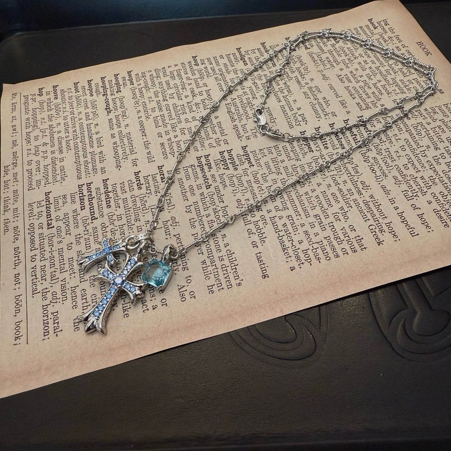 Silver cross pendant necklace with blue gemstone details laid on text pages