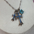 Close-up silver cross pendant with blue gemstones and dangling charm links
