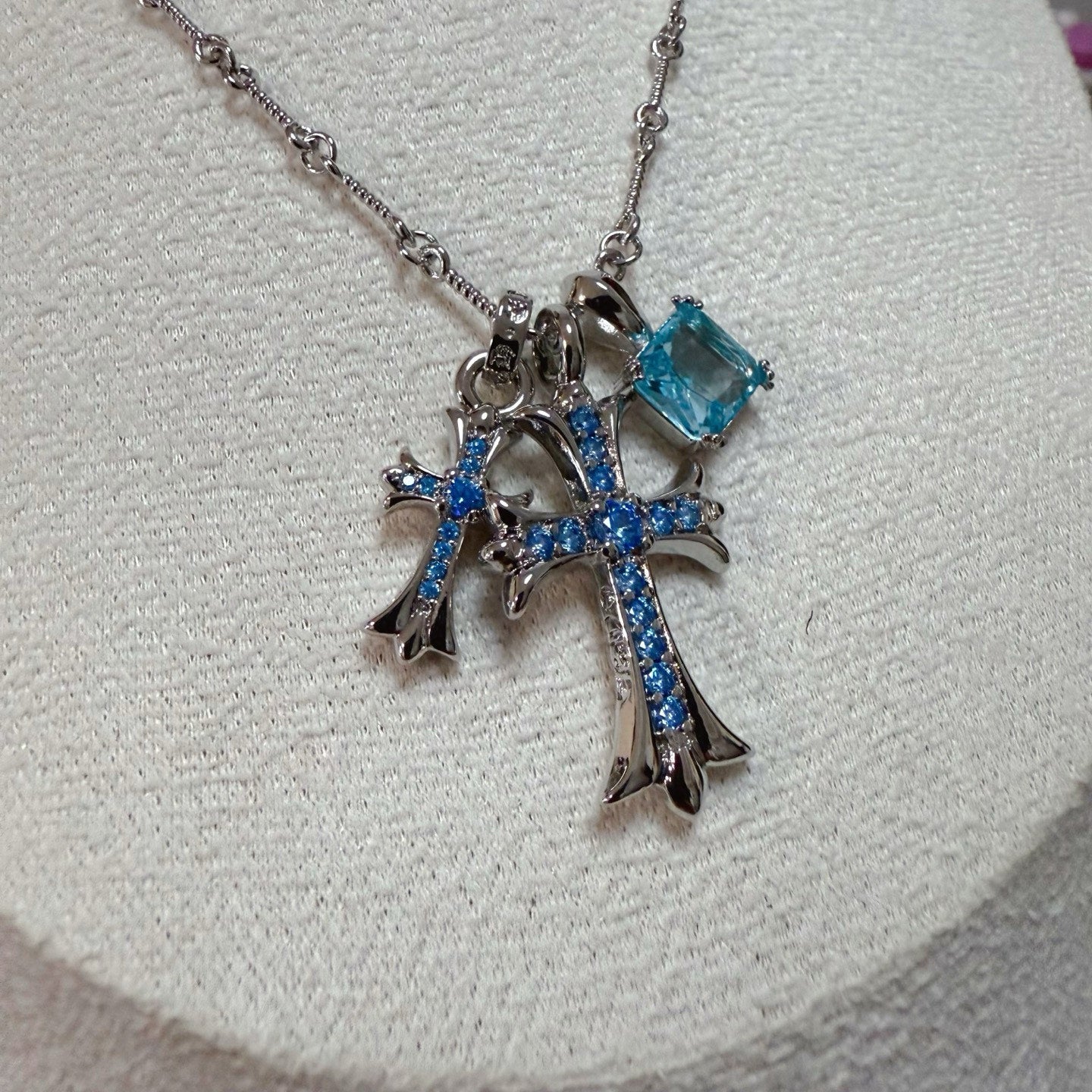 Close-up silver cross pendant with blue gemstones and dangling charm links