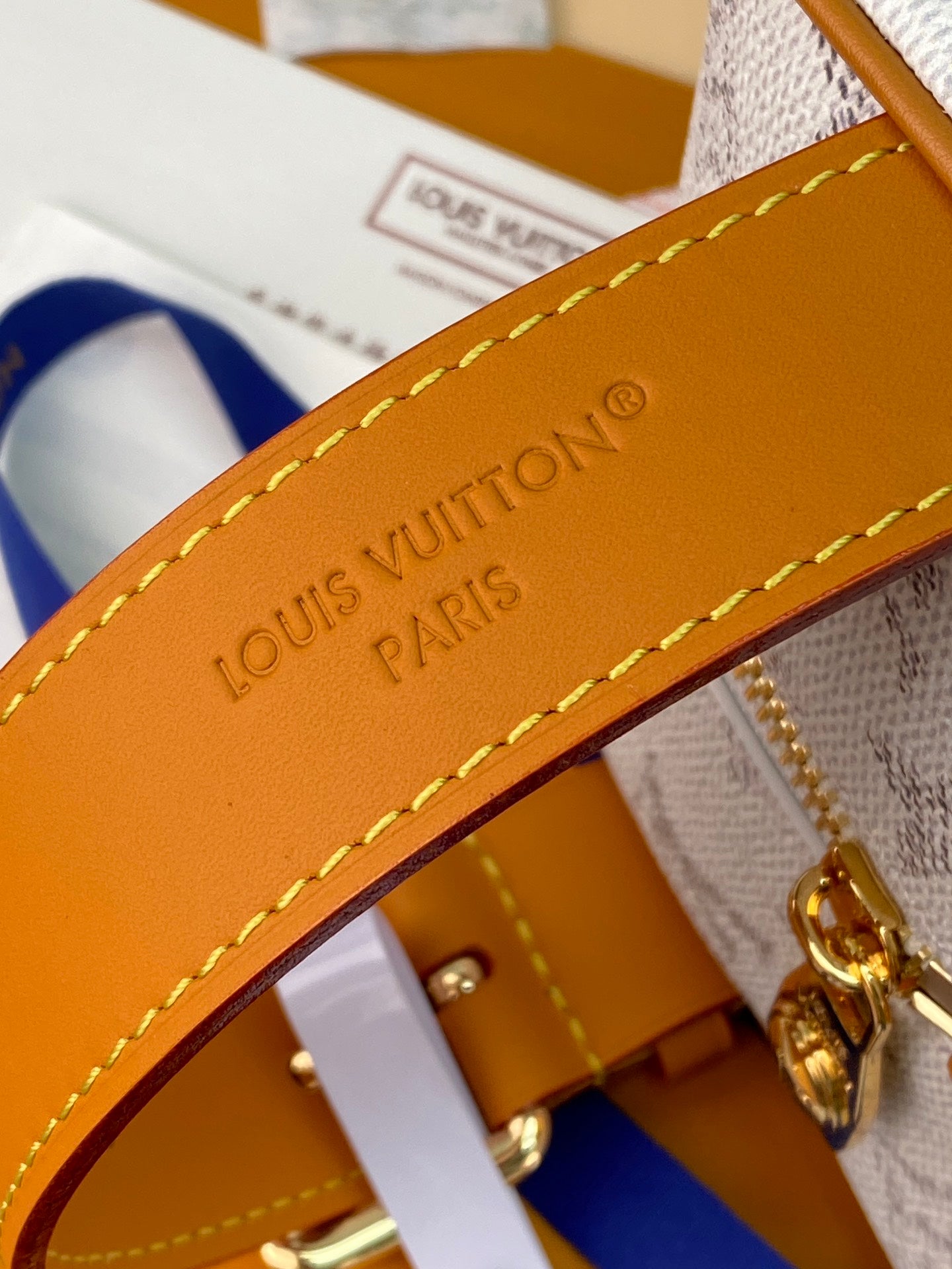 Louis Vuitton bag strap close-up, tan leather with yellow stitching and embossed lettering