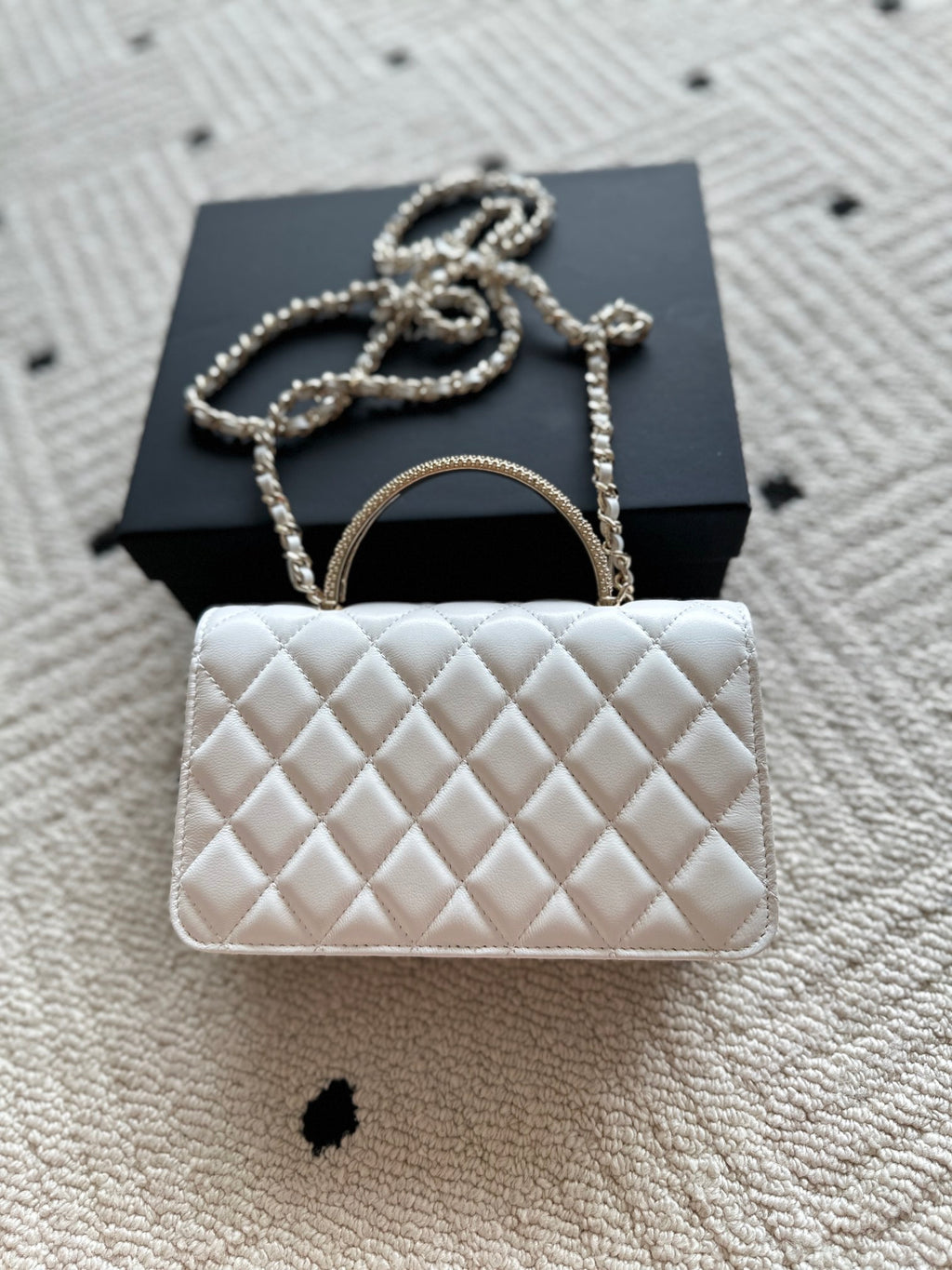 White quilted flap bag with gold-tone chain strap and rounded top handle.