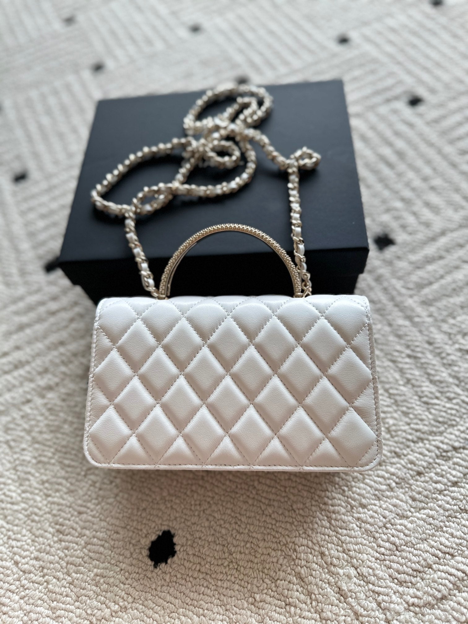 White quilted flap bag with gold-tone chain strap and rounded top handle.