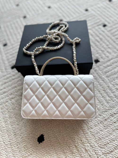 White quilted flap bag with gold-tone chain strap and rounded top handle.